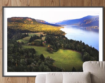 May include: An aerial photograph of a river winding through a lush green valley. The river is surrounded by trees and fields, and the sky is a soft blue. The photo is framed in a black frame and hanging on a wall.