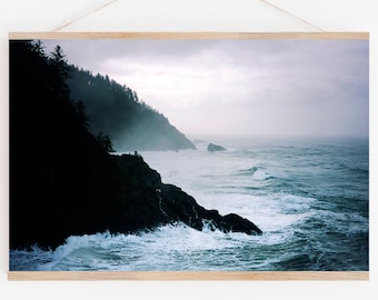 May include: A photograph of a rocky coastline with crashing waves and a misty forest in the background. The sky is overcast and the water is a deep blue.