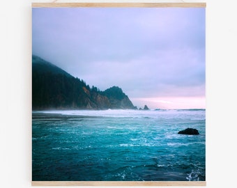 May include: A photograph of a misty, blue ocean with a rocky coastline in the background. The sky is a soft purple and the water is a deep turquoise.