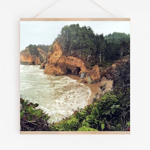 May include: A scenic photograph of a rocky coastline with a small waterfall cascading down a cliff face. Lush green trees line the cliff edge, and the ocean waves crash against the shore.