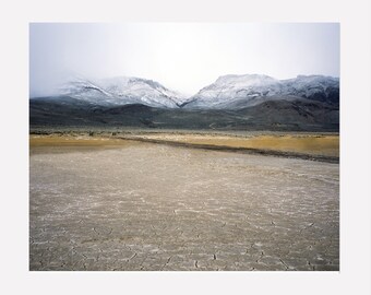 May include: A photograph of a dry, cracked lake bed with snow-capped mountains in the distance.