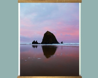 May include: A framed photograph of a large rock formation in the ocean at sunset. The rock is reflected in the water, and the sky is a mix of pink, purple, and orange.