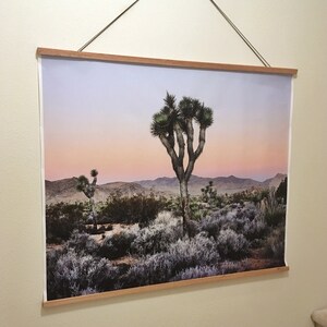 May include: A framed photograph of a Joshua Tree in the desert at sunset. The sky is a soft pink and purple, and the Joshua Tree is silhouetted against the mountains in the background.