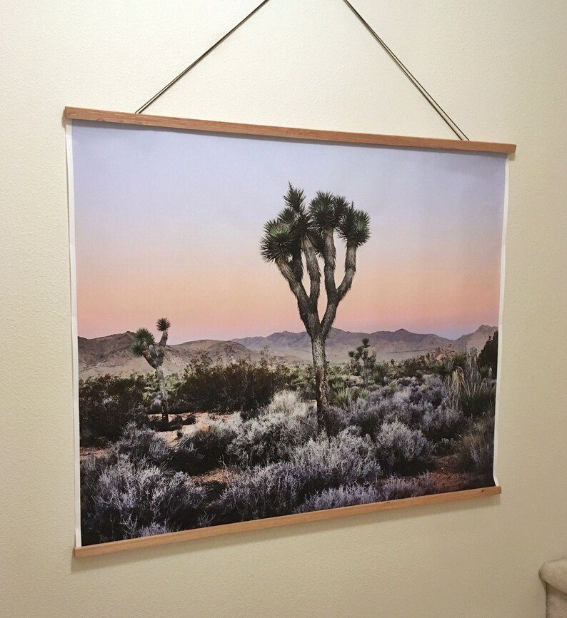 May include: A framed photograph of a Joshua Tree in the desert at sunset. The sky is a soft pink and purple, and the Joshua Tree is silhouetted against the mountains in the background.