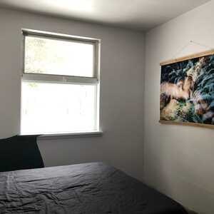 May include: A bedroom with a black bedspread, a window with white trim, and a framed print of a forest scene hanging on the wall.