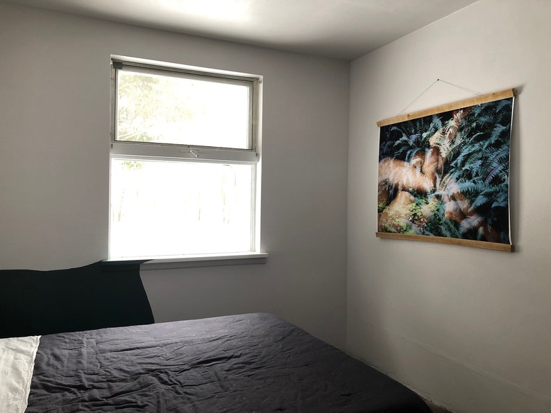 May include: A bedroom with a black bedspread, a window with white trim, and a framed print of a forest scene hanging on the wall.
