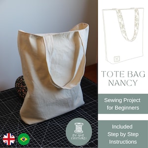 Pode incluir: Uma sacola tote bege, em pé sobre uma superfície preta. A sacola tem formato retangular com uma abertura larga e duas alças. O texto do lado direito diz "TOTE BAG NANCY" e "Sewing Project for Beginners".