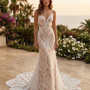 May include: A floor-length, sleeveless gown featuring a deep V-neckline and a fitted bodice. The dress is crafted from a nude-colored fabric overlaid with intricate white lace patterns in a repeating leaf-like design, ending in a train.