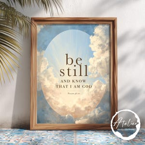 Può includere: Una stampa artistica da parete incorniciata che raffigura un cielo blu con nuvole bianche all'interno di una forma ovale. Il testo recita: be still AND KNOW THAT I AM GOD, Psalm 46:10. La cornice è in legno marrone chiaro con venature.
