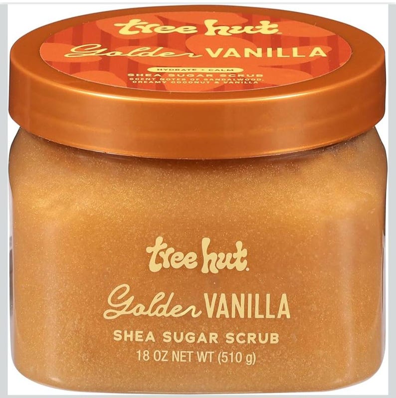 Puede incluir: Un tarro de exfoliante de az&uacute;car y karit&eacute; Tree Hut Golden Vanilla. El tarro tiene una tapa de bronce y un cuerpo transparente, lleno de un exfoliante marr&oacute;n dorado. La etiqueta presenta las palabras "Golden Vanilla" y "Shea Sugar Scrub", con un peso neto de 510 g.