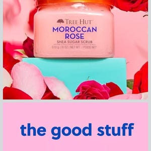 Puede incluir: Un tarro de exfoliante de az&uacute;car de karit&eacute; Tree Hut Moroccan Rose, 510 g, se encuentra sobre un bloque turquesa, rodeado de p&eacute;talos de rosa rosas y rosas rojas. El tarro tiene una tapa dorada y las palabras "the good stuff" debajo.