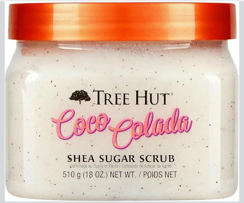Puede incluir: Un tarro de exfoliante de az&uacute;car de karit&eacute; Coco Colada de Tree Hut. El exfoliante blanco est&aacute; salpicado de motas oscuras y tiene una tapa de color naranja brillante. La etiqueta muestra el nombre de la marca, el nombre del producto y el peso neto de 510 g.