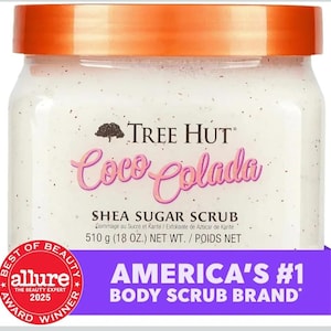Puede incluir: Un tarro de exfoliante de az&uacute;car de karit&eacute; Tree Hut Coco Colada. El exfoliante blanco est&aacute; en un tarro transparente con tapa naranja. La etiqueta presenta las palabras "Coco Colada" en rosa y "America's #1 Body Scrub Brand".