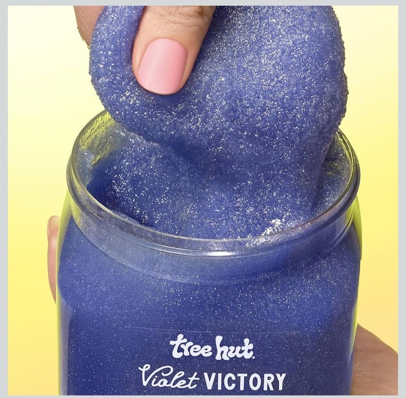 Puede incluir: Un tarro de exfoliante corporal Tree Hut Violet Victory. El exfoliante es de color violeta intenso con una textura brillante. El tarro es transparente y la etiqueta presenta el nombre de la marca y del producto en escritura blanca.