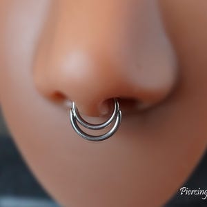 May include: A silver-coloured titanium double-layered septum ring featuring two smooth, circular hoops stacked together. The text 'Titanium' appears in the top left corner and 'Piercing Queen' is written in the bottom right corner of the image.