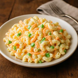 Peut inclure: Une assiette de salade de macaroni avec des macaronis coudés, des carottes oranges et du céleri vert coupé en dés. Les macaronis sont enrobés d'une sauce crémeuse jaune pâle. La salade est servie dans une assiette blanche.