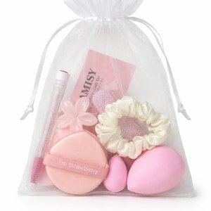 Può includere: Un sacchetto in organza bianco trasparente con coulisse contenente accessori di bellezza rosa. Include un piumino da cipria rosa con la scritta I'm Strowberry, una clip rosa a forma di fiore, un elastico in raso bianco, due spugnette per il trucco rosa e uno scovolino per mascara rosa.