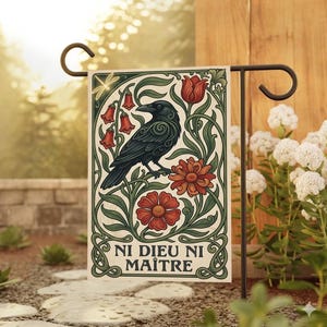 Può includere: Una bandiera da giardino decorativa con un corvo nero posato su un ramo, circondato da fiori rossi e fogliame verde. La bandiera presenta il testo "NI DIEU NI MAÎTRE" in un carattere decorativo. Montata su un supporto in metallo nero.