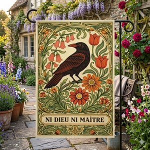 May include: A rectangular garden flag with a crow illustration, surrounded by orange and red flowers and green foliage. The flag has the text "NI DIEU NI MAÎTRE" at the bottom. The flag is displayed in a garden setting.