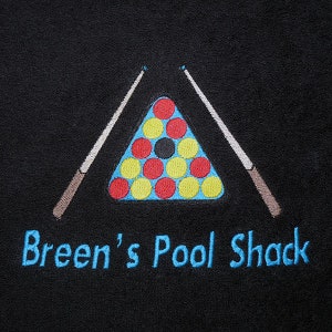 Könnte beinhalten: Schwarze bestickte Billardtisch mit einem Dreieck von Billardkugeln und zwei Queues. Der Text "Breen's Pool Shack" ist unter dem Tisch gestickt.