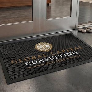 May include: Black rectangular doormat with the text "GLOBAL CAPITAL CONSULTING EST. 2022" in gold and white. The mat has a textured surface and a black border. A decorative emblem is at the top.