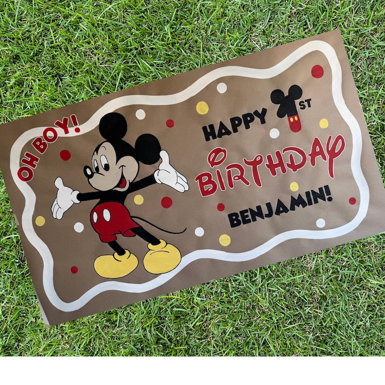 May include: A brown banner featuring Mickey Mouse with the text "Happy Birthday Benjamin!" in red and black. The banner has a white border and red, white, and yellow polka dots. Mickey Mouse is wearing red shorts and yellow shoes.