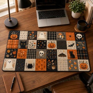 May include: A rectangular desk mat featuring a patchwork grid design with Halloween-themed illustrations including orange pumpkins, white ghosts, black cats, skulls, moths, bats, mushrooms, and autumn foliage in a color palette of orange, black, and cream.