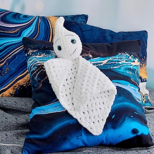 May include: A white crocheted ghost lovey featuring a soft, plush texture with a rounded head, embroidered facial features including dark eyes and a small smile, and a textured, triangular-shaped blanket body with a repeating stitch pattern.