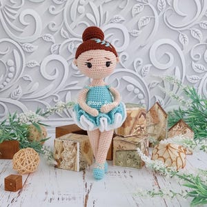 May include: A crocheted ballerina doll with a brown bun hairstyle, wearing a light blue bodice and a layered blue and white tutu. The doll has embroidered facial features and light blue ballet slippers. The text @toys_funny is visible on the bodice.