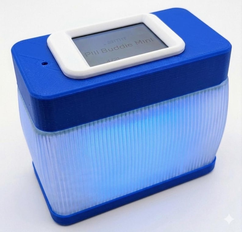 Puede incluir: Un dispositivo Pill Buddie Mini azul y blanco. La parte superior es azul con una pantalla rectangular blanca que muestra texto. La secci&oacute;n inferior es un dise&ntilde;o transl&uacute;cido y acanalado que brilla con luz azul.