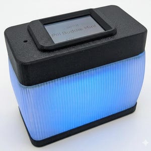 Puede incluir: Un dispositivo rectangular negro con una peque&ntilde;a pantalla que muestra "Pill Buddie Mint". La parte inferior del dispositivo brilla con una luz azul brillante. El dispositivo tiene un cuerpo transl&uacute;cido y acanalado.