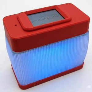 Puede incluir: Un dispositivo rectangular rojo con una peque&ntilde;a pantalla que muestra "Pill Buddie Mini". La mitad inferior es transl&uacute;cida con l&iacute;neas verticales, iluminada por una luz azul. Dise&ntilde;o moderno.