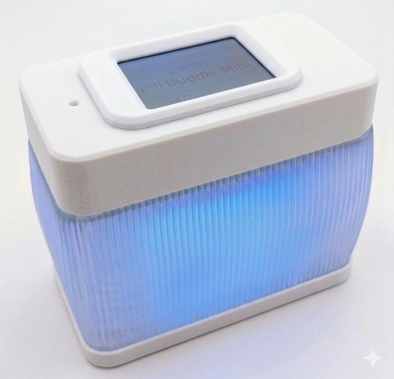 Puede incluir: Un dispositivo blanco y rectangular con una peque&ntilde;a pantalla que muestra texto, etiquetado como "Pill Buddie Mini". La parte inferior del dispositivo es transl&uacute;cida con ranuras verticales, iluminada por una suave luz azul. Dise&ntilde;o moderno y minimalista.
