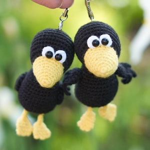 May include: Two handmade crochet bird charms. Each bird has a black body, yellow beak and feet, and large white eyes. The charms are attached to silver keychains, ideal for a backpack or purse.