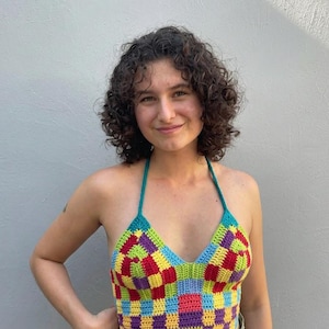 May include: A halter top featuring a vibrant, multi-colored checkered pattern in shades of yellow, red, blue, green, and purple. The garment is constructed from crocheted yarn, showcasing a V-neckline and thin straps that tie behind the neck.