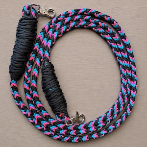 May include: A black, neon pink, and blue braided rope with two silver metal clasps. The rope is coiled in a circular pattern. The ends of the rope are wrapped in black material.