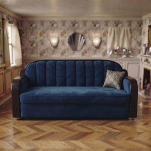 May include: A deep blue velvet sofa featuring a channel-tufted backrest and dark wood armrests. The sofa includes a single square throw pillow with a gold and black fan-shaped pattern, positioned on the right side of the seat cushion.