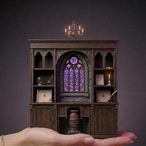 May include: A miniature wooden bookshelf diorama featuring a central arched stained glass window with purple light, side shelves holding small books, a crystal ball, inkwells, and a quill, topped with a small chandelier and a base stove.