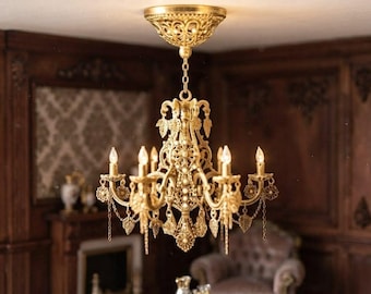 May include: A gold-toned chandelier featuring six candle-style lights, intricate filigree metalwork, and delicate hanging chain accents. The fixture is suspended from a matching ornate ceiling canopy by a central chain, showcasing a detailed design.