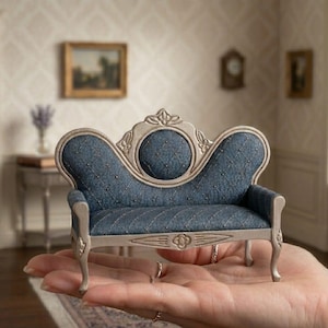 May include: A miniature dollhouse sofa featuring a silver-toned frame with ornate carved details and a blue fabric upholstery. The backrest has a central circular panel and a diamond-tufted pattern accented with small metallic studs throughout.