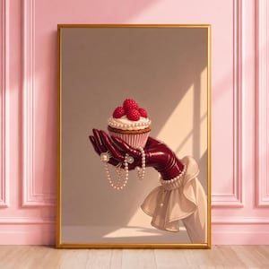 May include: A framed wall art print depicting a hand wearing a glossy dark red glove and a ruffled beige cuff, holding a cupcake topped with fresh raspberries and a pearl necklace draped over the fingers, set against a neutral background.