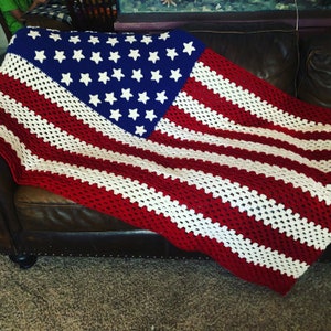 May include: A crocheted American flag blanket in red, white, and blue. The blanket is draped over a brown leather couch.