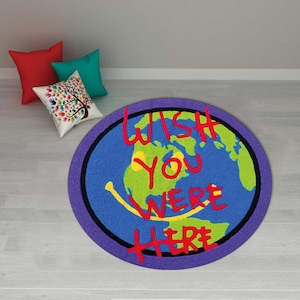 May include: A round rug with a blue background depicting a world map with green continents and a yellow smiley face. The words "WISH YOU WERE HERE" are written in red. A purple border surrounds the rug.