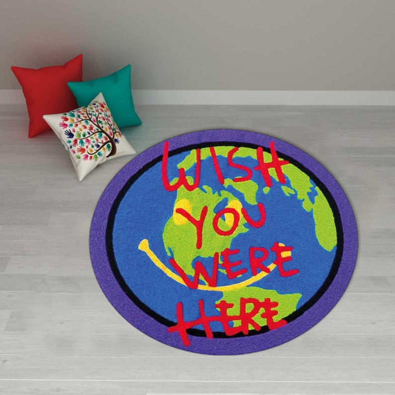 May include: A round rug with a blue background depicting a world map with green continents and a yellow smiley face. The words "WISH YOU WERE HERE" are written in red. A purple border surrounds the rug.