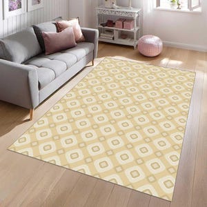 May include: A rectangular area rug featuring a repeating geometric pattern of rounded squares in shades of beige, cream, and light brown. The rug is laid flat on a light-coloured wooden floor, displaying a consistent grid of soft-edged square shapes.