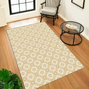 May include: A rectangular area rug featuring a repeating geometric pattern of rounded squares in shades of beige, cream, and light brown. The rug is laid flat on a wooden floor, showcasing a consistent grid design across its entire surface area.