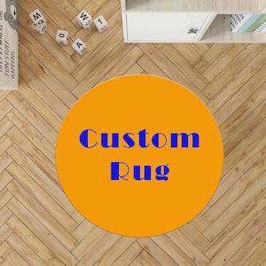 May include: An orange circular rug with the words "Custom Rug" in blue. The rug is on a light brown wooden floor. The image also shows a white shelf and some decorative blocks.