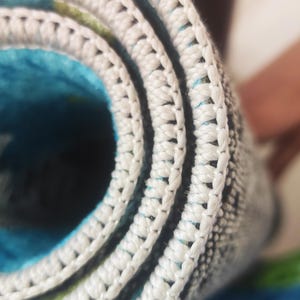 May include: Close-up of a rolled-up rug with a white, textured border. The rug's interior features a vibrant blue and green pattern. The white border is made of a thick, woven material.
