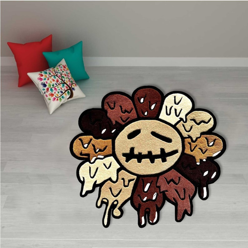May include: A unique, decorative rug in the shape of a sunflower with a distressed face design. The rug features a variety of brown and beige tones, with a black outline. The rug is placed on a light-colored wooden floor. Three throw pillows are in the background.