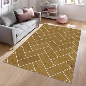 May include: A rectangular area rug featuring a repeating herringbone pattern in a textured golden-brown hue with thin white lines separating each rectangular block. The design covers the entire surface of the rug, creating a geometric layout.
